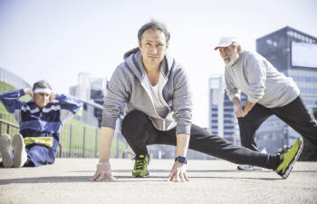 Three middle-aged men stretching as a part of their warmup before a run.