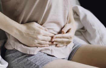 A woman sitting on the bed suffering from abdominal pain.